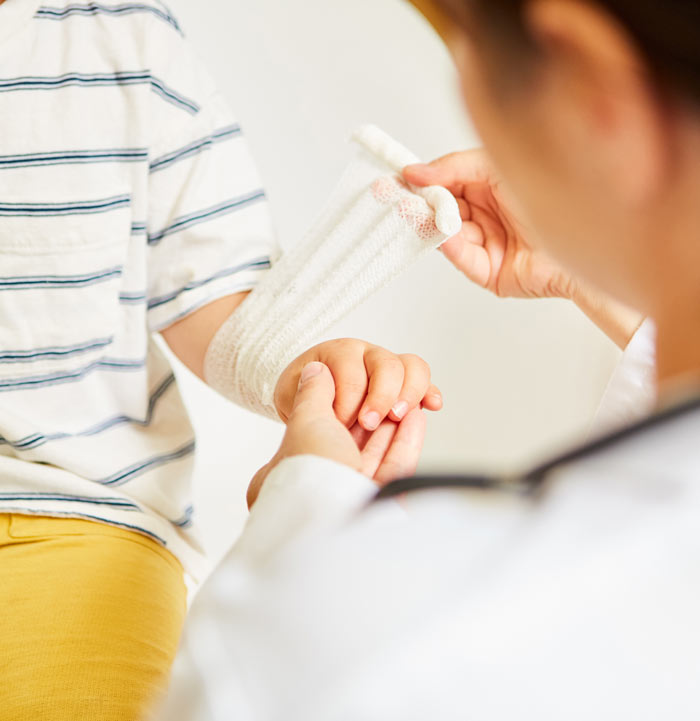 A child receiving medical care as a healthcare professional wraps a bandage around the child's arm.