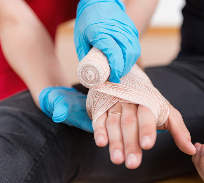 A person in blue gloves is wrapping a bandage around an injured hand, focusing on proper first aid techniques.