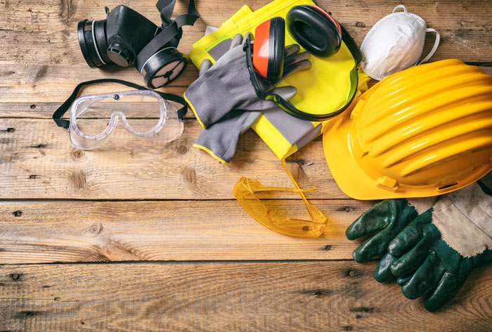 safety gear arrangement featuring a hard hat, protective goggles, gloves, ear protection, and a dust mask on a wooden surface